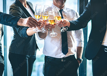 A group of businessmen and businesswoman wearing formal clothes, holding champagne glasses and having a toast